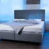 Eine Bodypur-Matratze und Kopfkissen arrangiert auf einem Bett mit grauem Kopfteil und blauen LED-Leuchten im Hintergrund, was eine beruhigende Schlafumgebung suggeriert.
